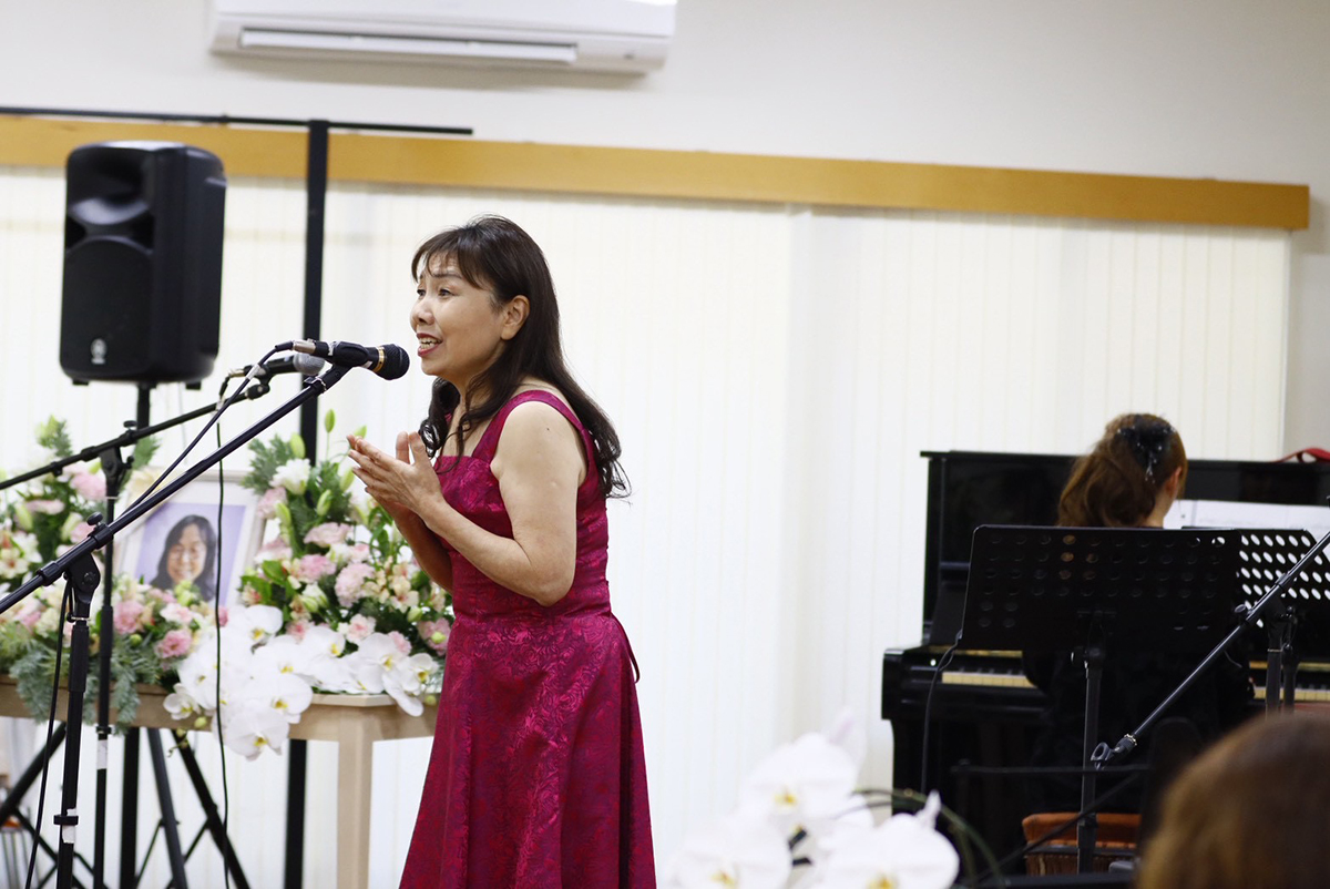 花に囲まれたステージ、歌う中島則子さん